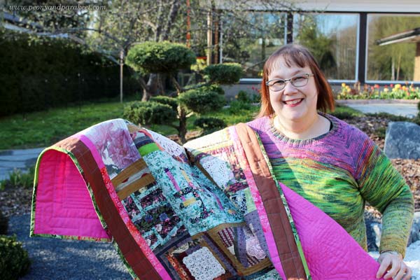 Paivi Eerola from Peony and Parakeet holding her hand-made quilt.