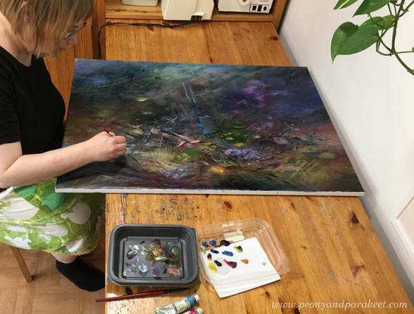 Paivi Eerola sitting in her studio and painting an oil painting. Read more about her mystical art.